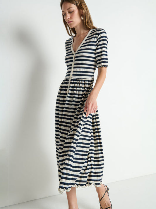 Woman in a navy and white striped crinkle midi dress with black sandals, walking indoors.