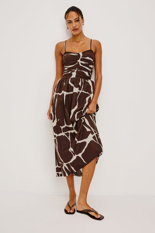 Brown and white abstract maxi dress with adjustable straps, displayed on a woman against a plain white backdrop.