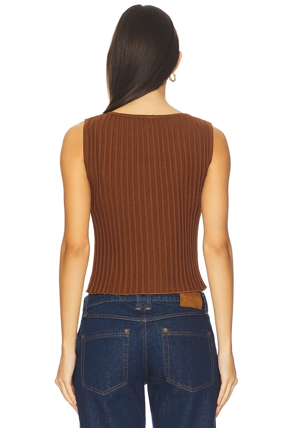 Back view of woman in honey bronze quilted vest and dark blue jeans, long dark hair visible. Casual outerwear style.