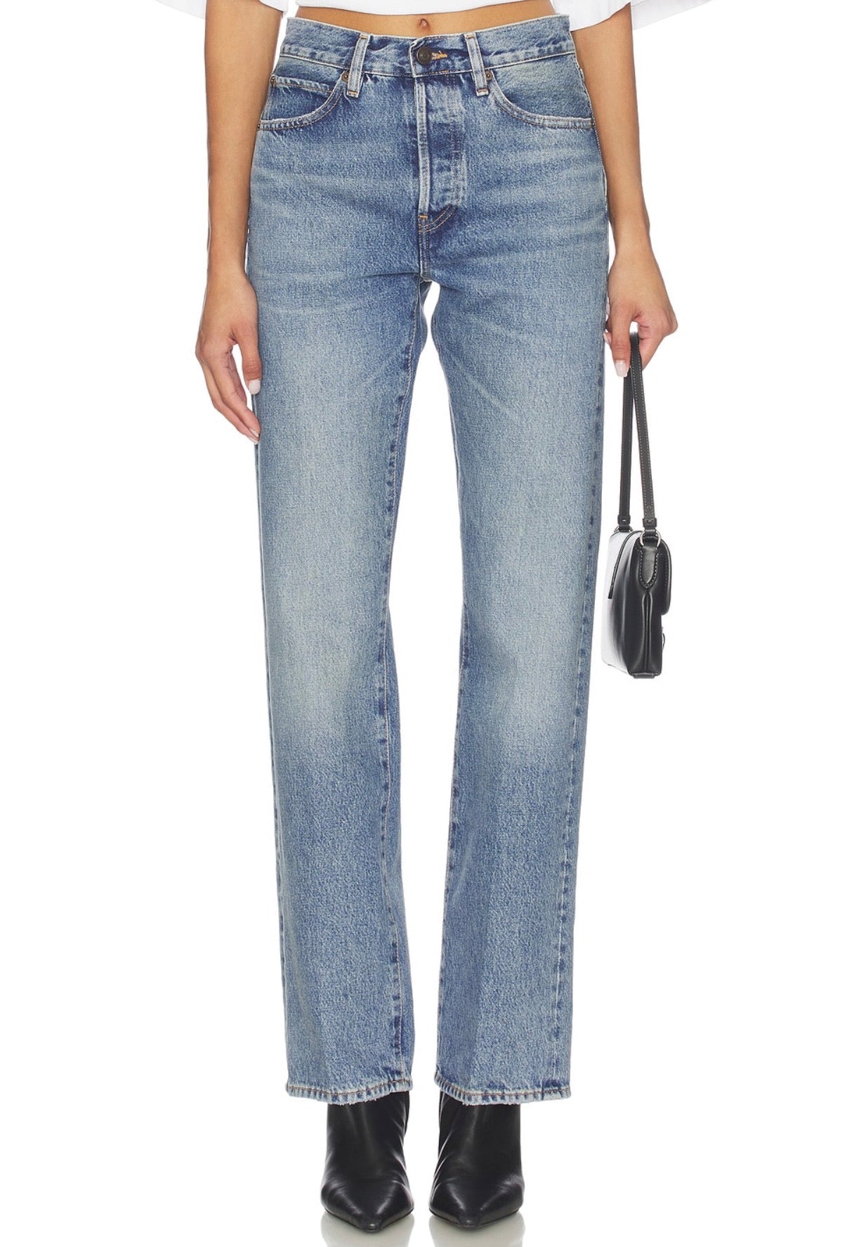 Person in high-waisted blue jeans, black boots, and carrying a small black leather handbag.