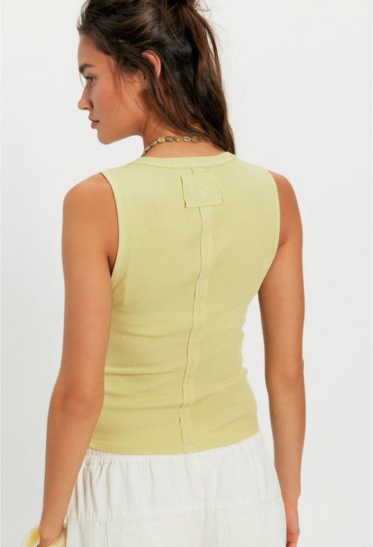 Woman in yellow Sicilian cotton tank and white pants, brown hair in a loose ponytail, shown from the back.