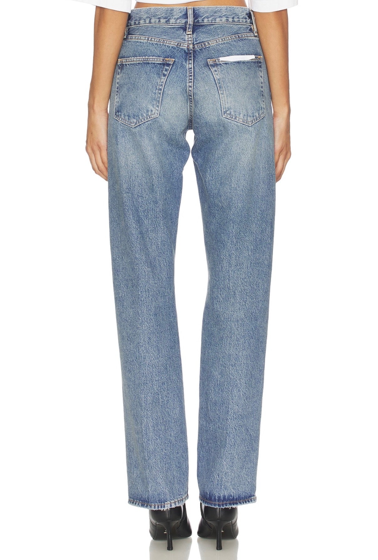 Back view of blue denim jeans paired with black heels, shown on a plain background.