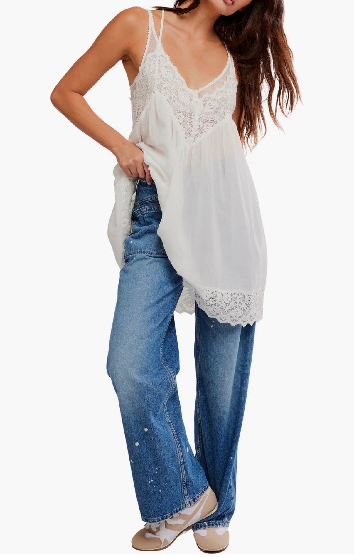 Woman wearing ivory slip dress and wide-leg blue paint-splatter jeans with beige shoes.