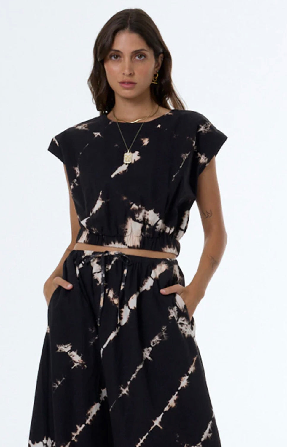 Woman in tie-dye Wendy top with hands in pockets, plain backdrop; casual wear, lightweight fabric, relaxed fit.