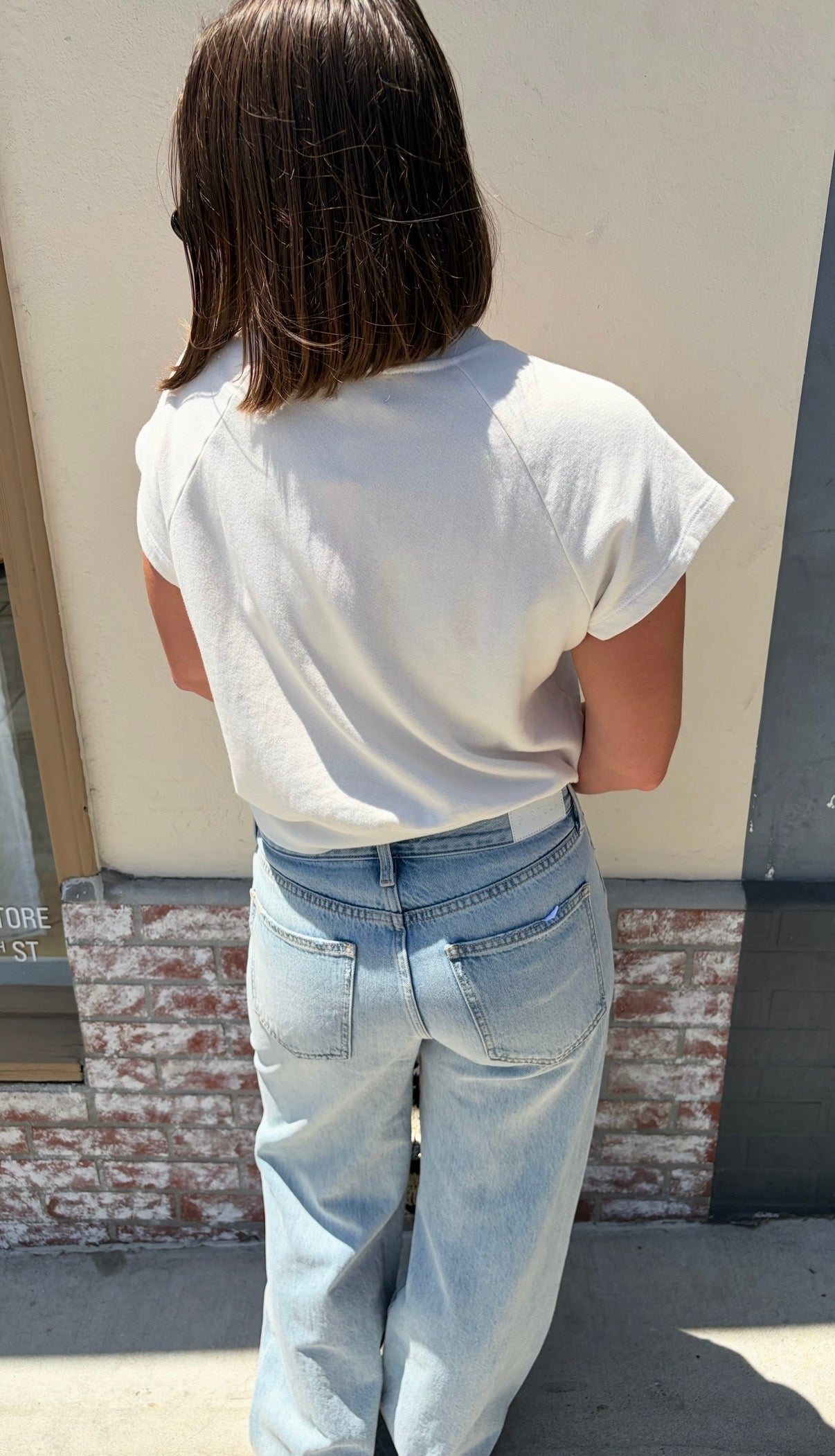 Person outdoors in a pearl-colored cotton sweatshirt with “J’adore Le Soleil” print, shoulder-length brown hair.