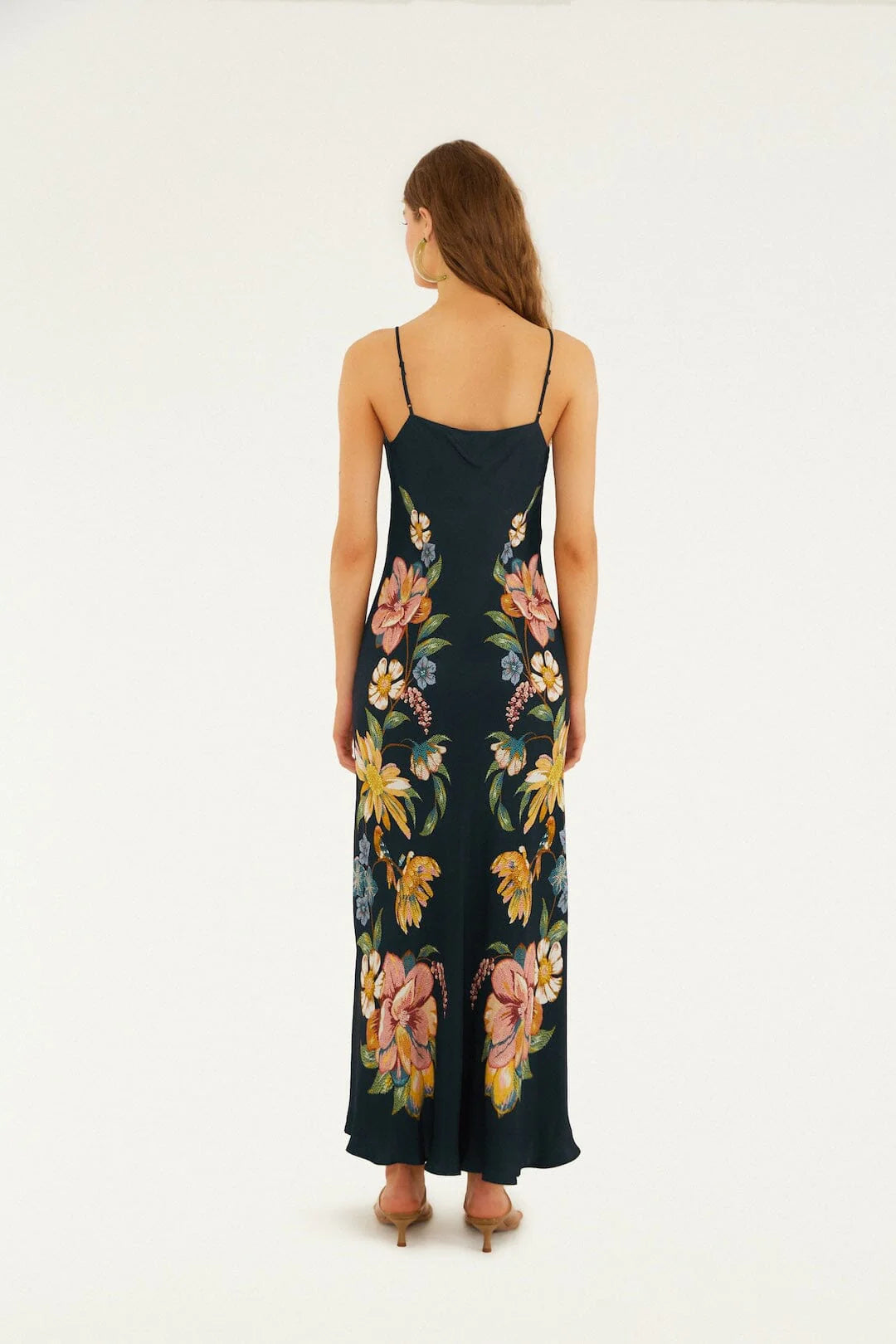 Woman in dark blue floral maxi dress, barefoot, shown from behind against a plain white background.