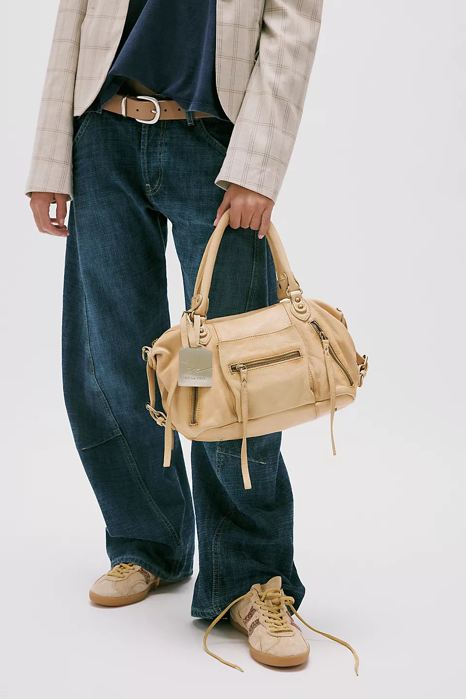 Butter yellow leather shoulder bag carried by person in wide-leg jeans, checked blazer, and tan sneakers.