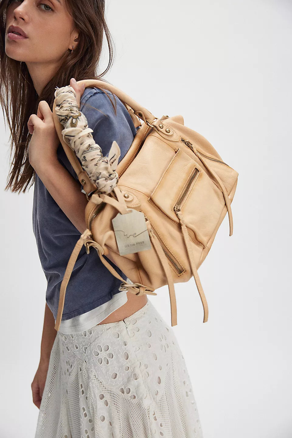 Woman in blue shirt and white skirt carries butter yellow leather shoulder bag with scarf-wrapped handle.