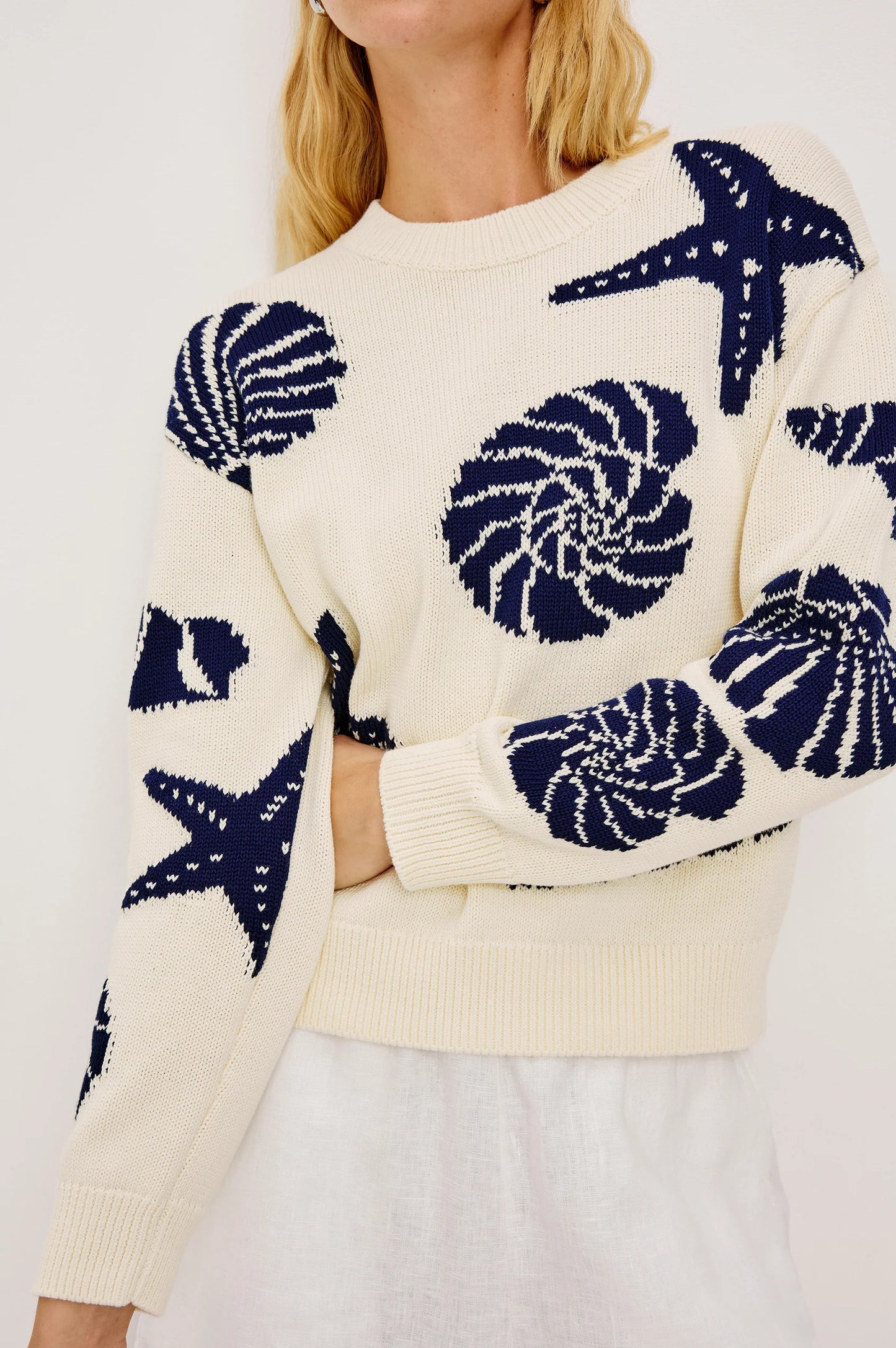 Woman in a light-colored knit sweater and white skirt, showcasing seashell-toned fabric ideal for cool weather layering.