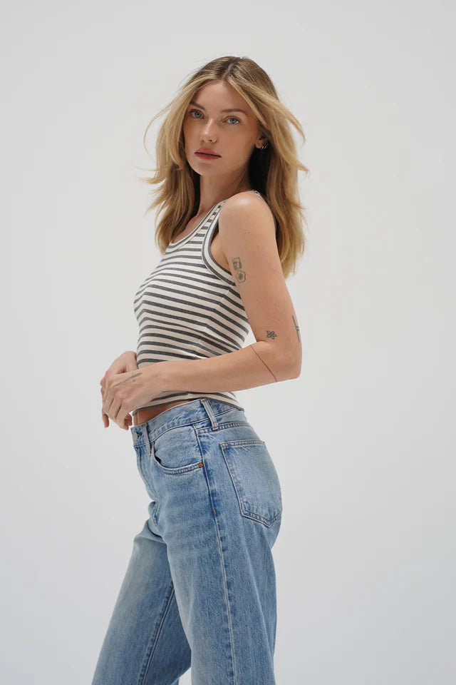 Woman wears a greyscale striped knit tank and blue jeans, standing against a white background, facing the camera.