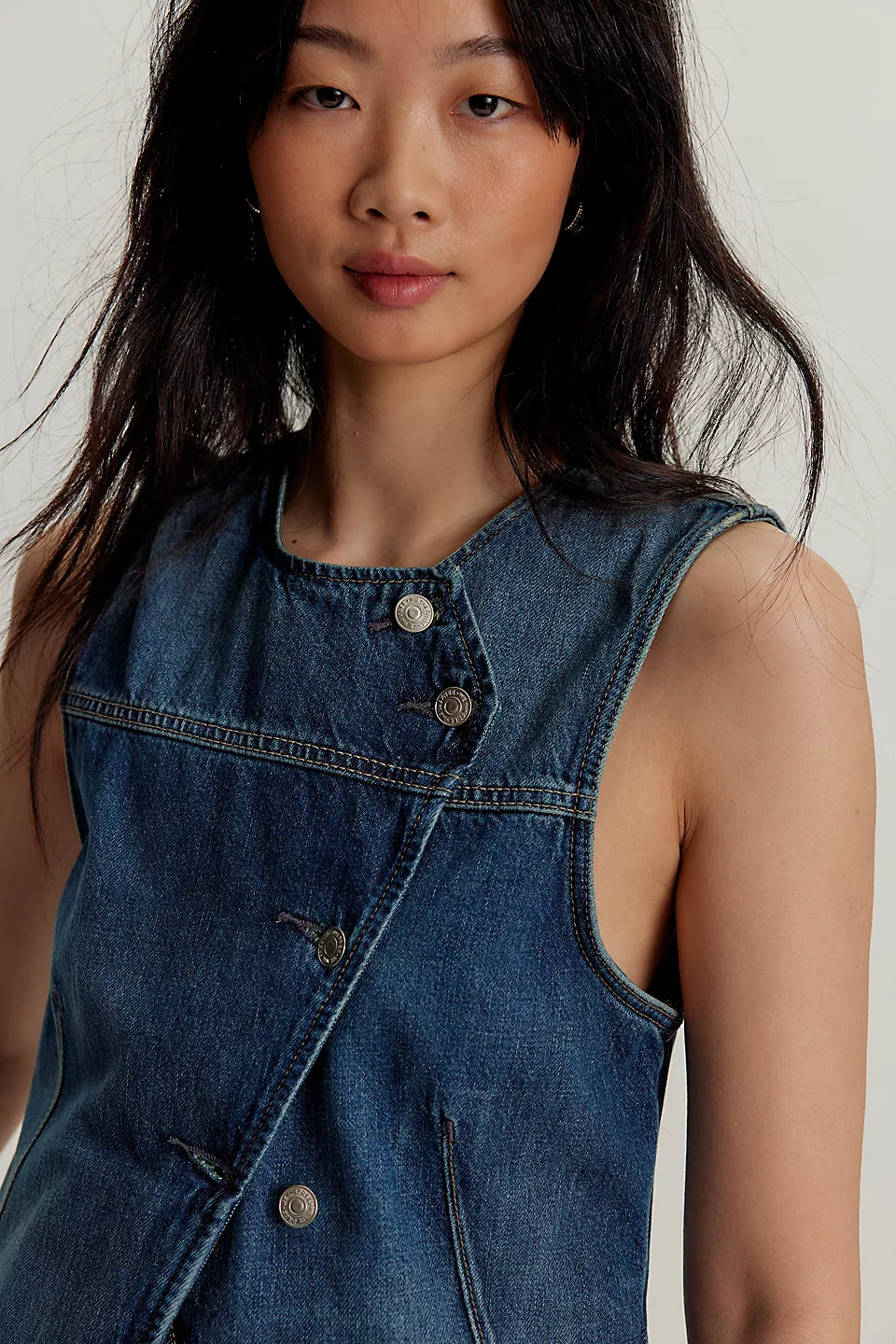 Woman with long dark hair wears a light blue denim vest made of cotton, facing the camera.