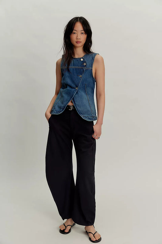 Woman in blue denim vest, wide-leg black pants, and black sandals stands against a plain background.