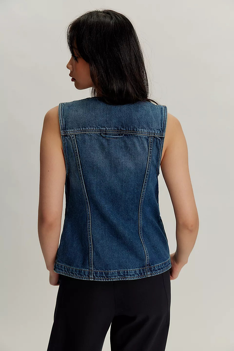 Back view of person with long dark hair wearing a light blue denim vest, shown against a plain background.