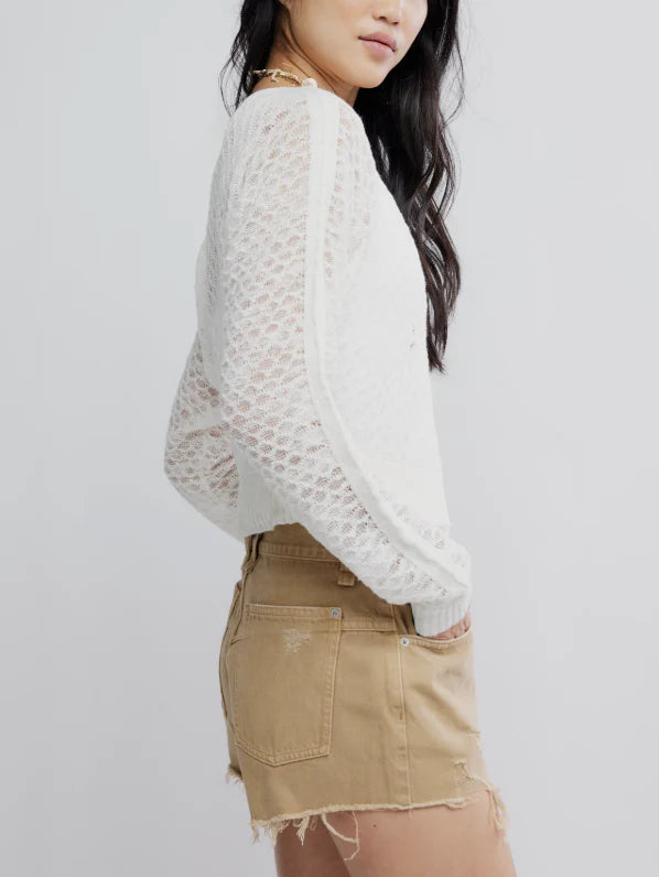 Woman wears an ivory fine gauge cardigan, shown from the side against a plain light background. Sweater is lightweight and knit.