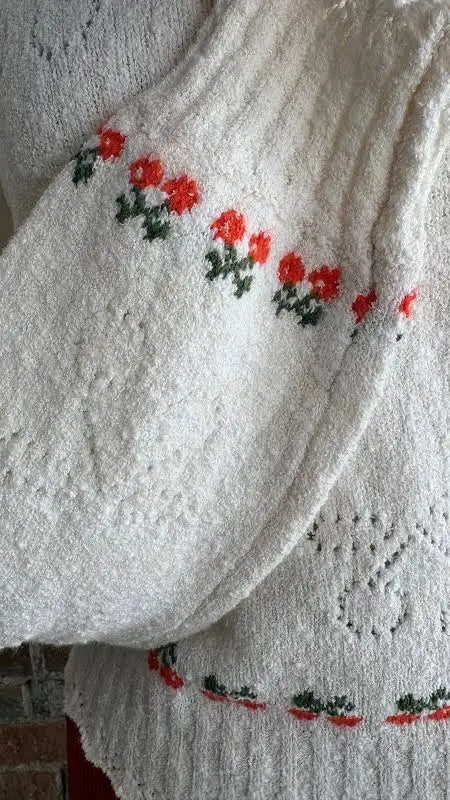 Ivory pullover with cherry and green floral embroidery on sleeve and hem, knit fabric ideal for casual wear.
