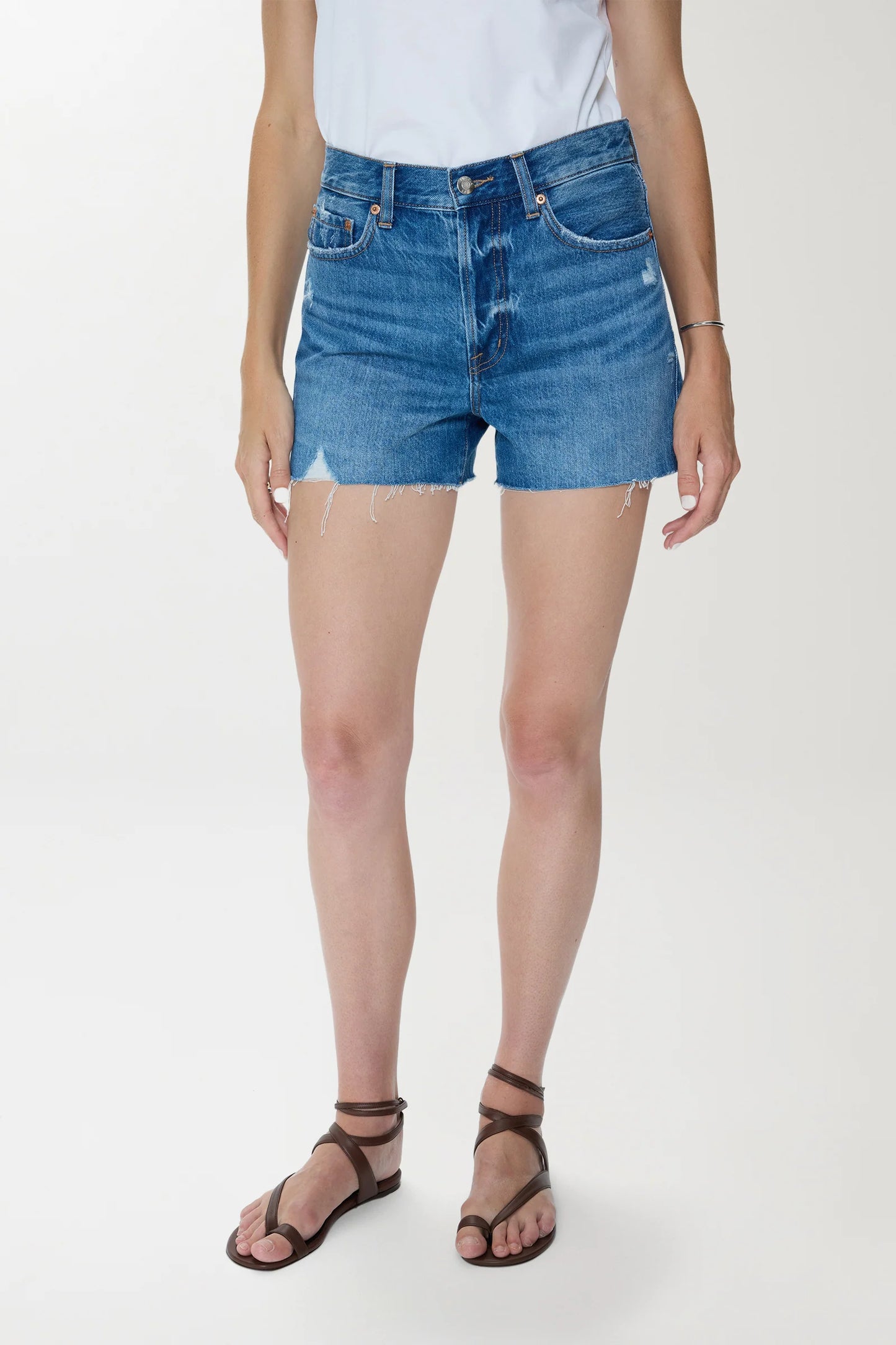 Woman in light denim high-rise cutoff shorts and a white cotton t-shirt, standing against a plain background.