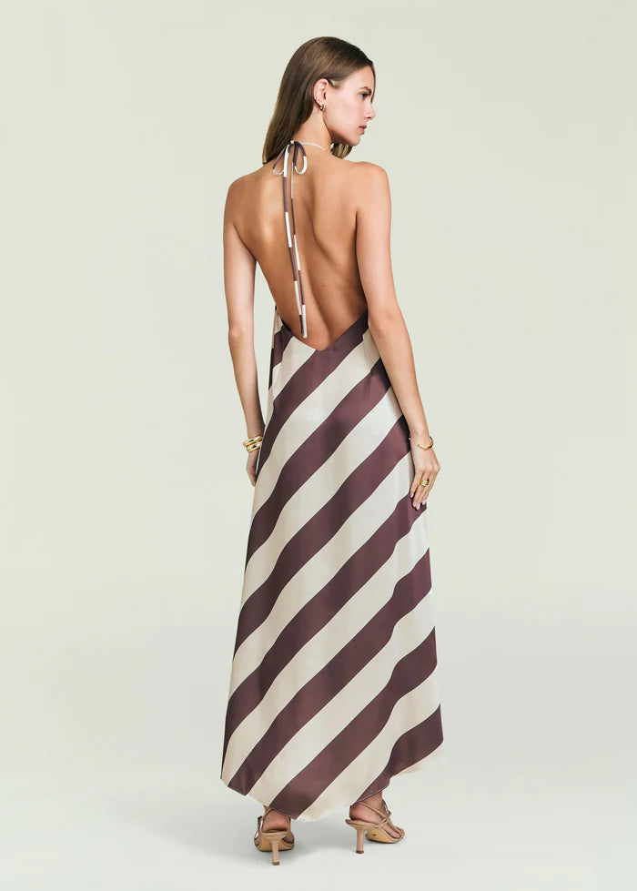 Backless halter-neck maxi dress in brown and beige stripes, worn with heeled sandals; model faces away.