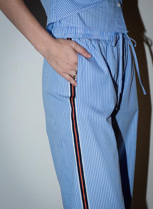Blue and white pinstripe relaxed fit pants with black and red side stripe, shown with hand-in-pocket. Cotton blend for casual wear.