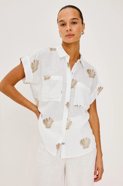 Taupe seashell print button-down shirt paired with white pants, shown on a woman against a plain background.