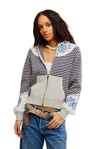 Woman wearing a grey zip-up jacket over a white top, jeans, and a chunky beaded necklace.