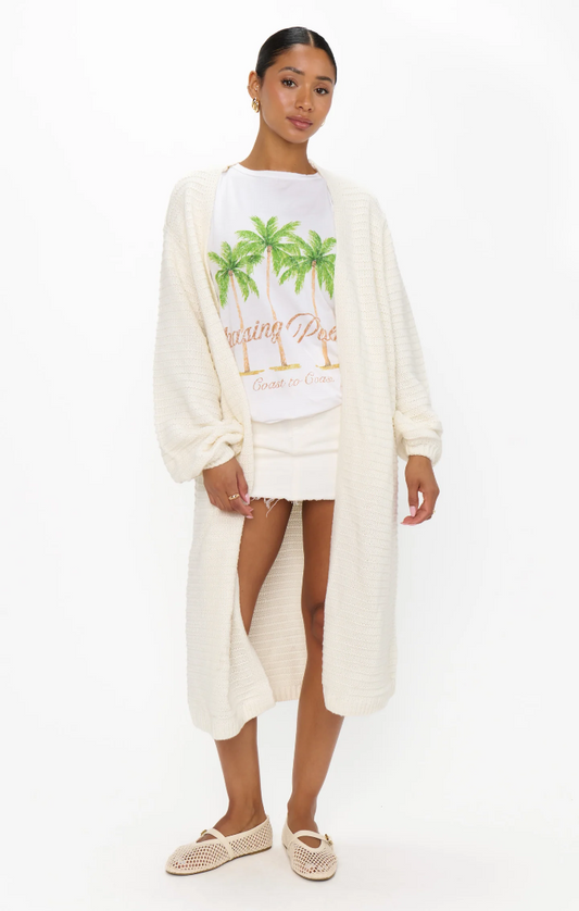 Woman in a buttercream knit cardigan, white shorts, palm print tee, and woven shoes for casual wear.