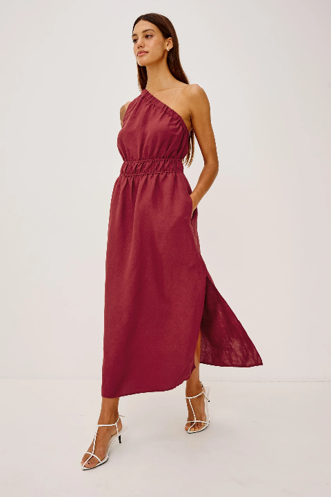 A woman models a spice-colored dress with white heels, standing in front of a simple white background.