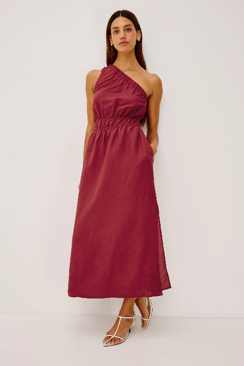 Woman wears a spice-colored midi dress with white strappy heels, shown against a simple, neutral background.