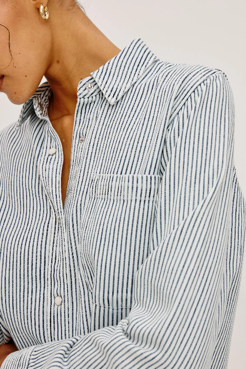 Woman wearing a striped cotton button-up shirt with gold hoop earrings, hair loosely framing her face.
