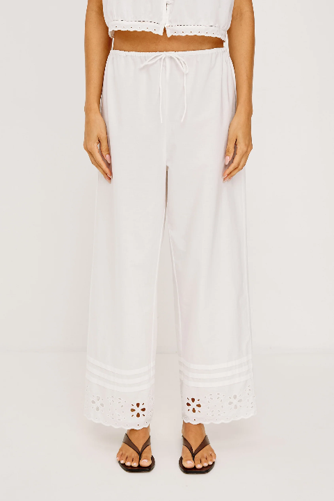 Woman models white drawcord linen pants with lace trim, matching top, and black sandals against a plain white background.