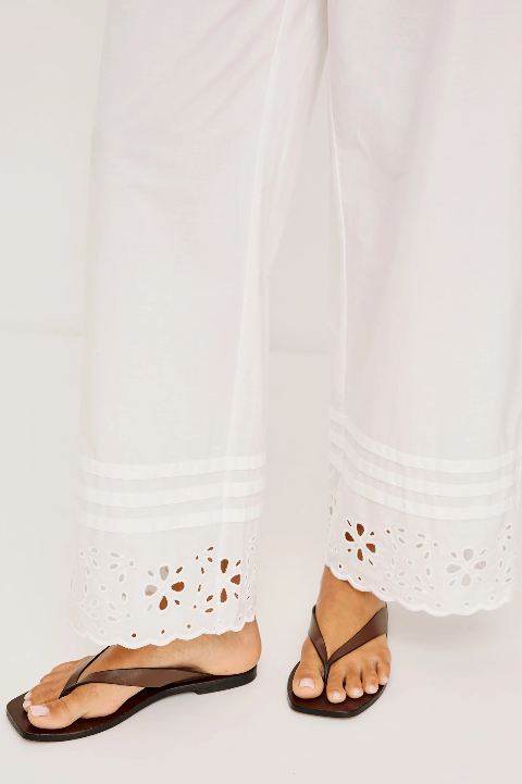 White linen pants with black flip-flops on a pale floor, showcasing lightweight, casual wear suitable for warm weather.