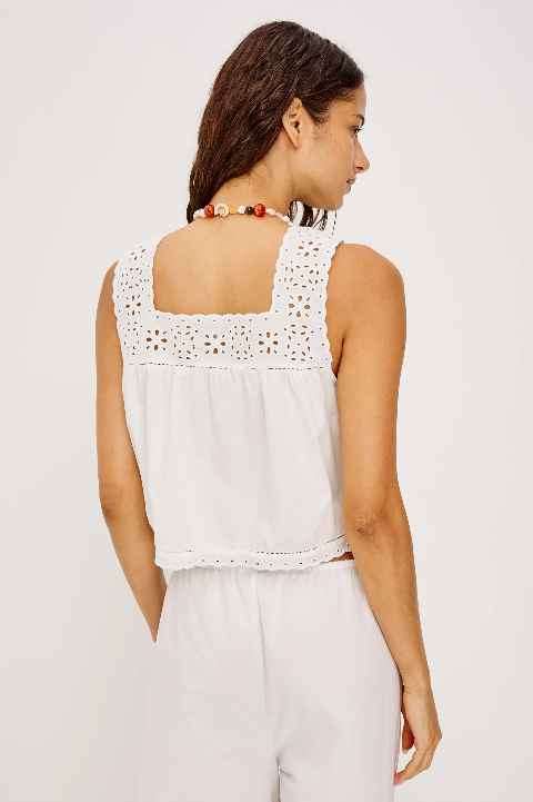 Woman wearing white embroidered-strap top, white pants, and beaded necklace, shown from the back.