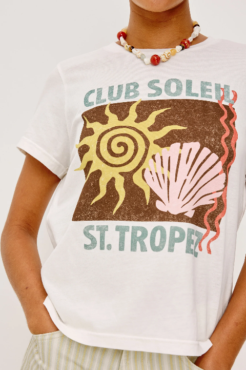 Person wearing a cropped beige cotton crewneck tee with sun and shell graphics, paired with a beaded necklace.