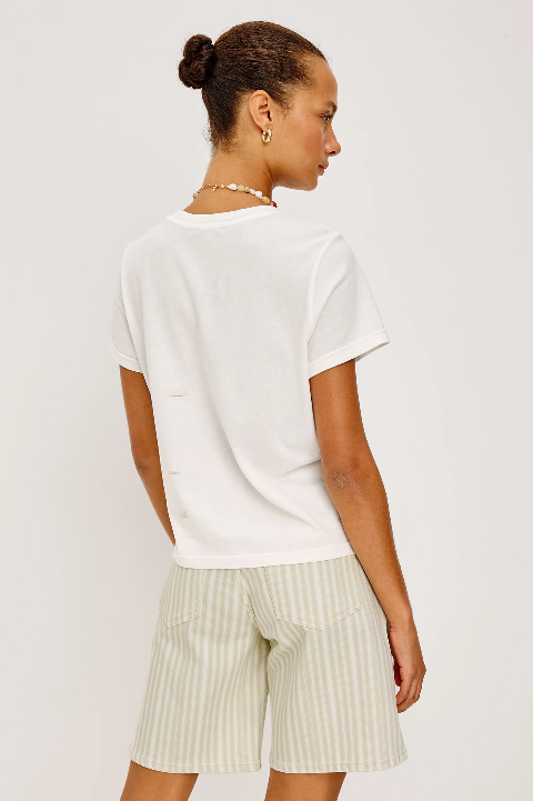 Woman in a cropped beige crewneck tee and striped cotton shorts; hair in bun, standing against a plain background.