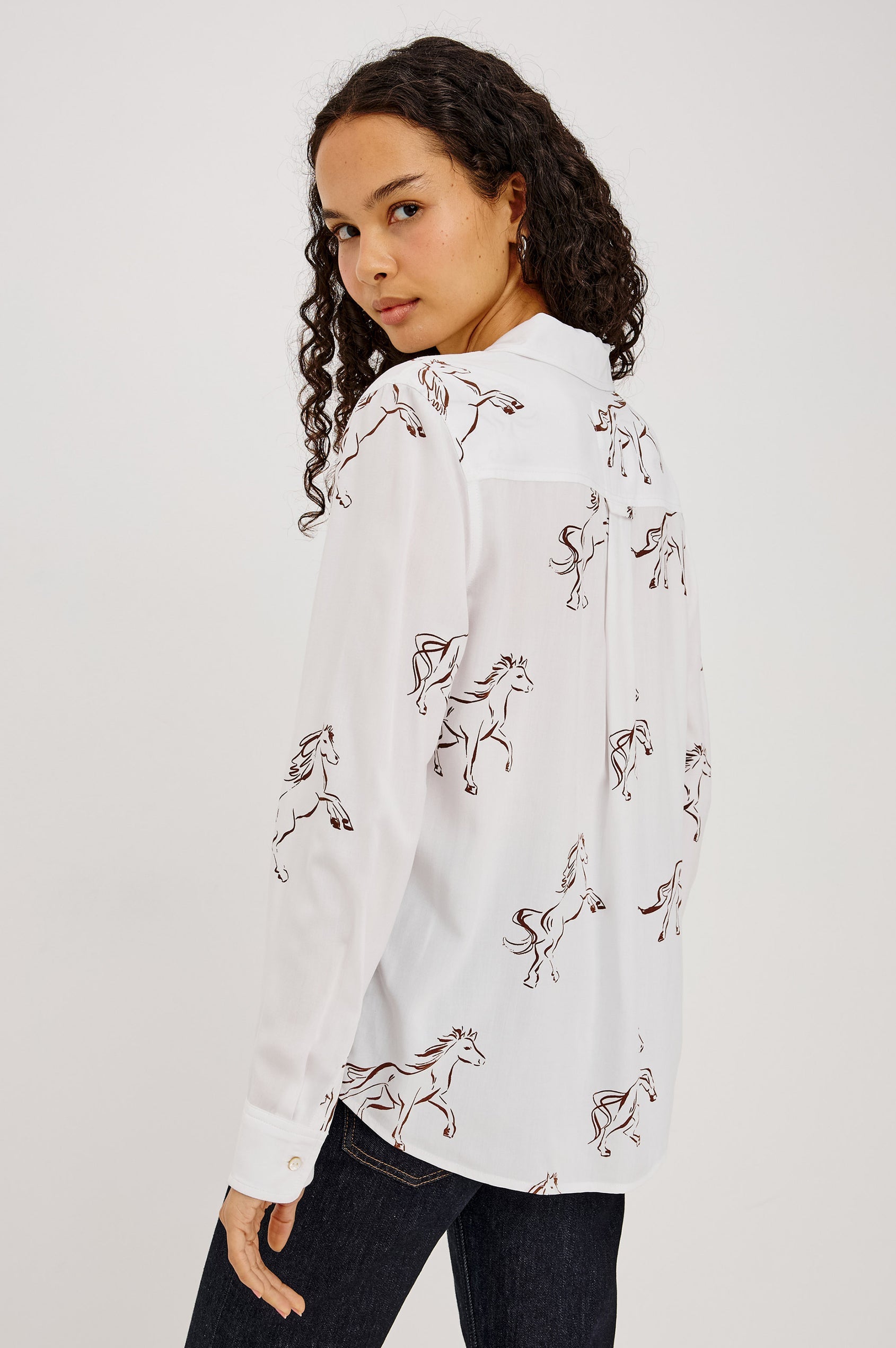 A woman wearing a white long-sleeve button-up shirt with an allover embroidered horse pattern