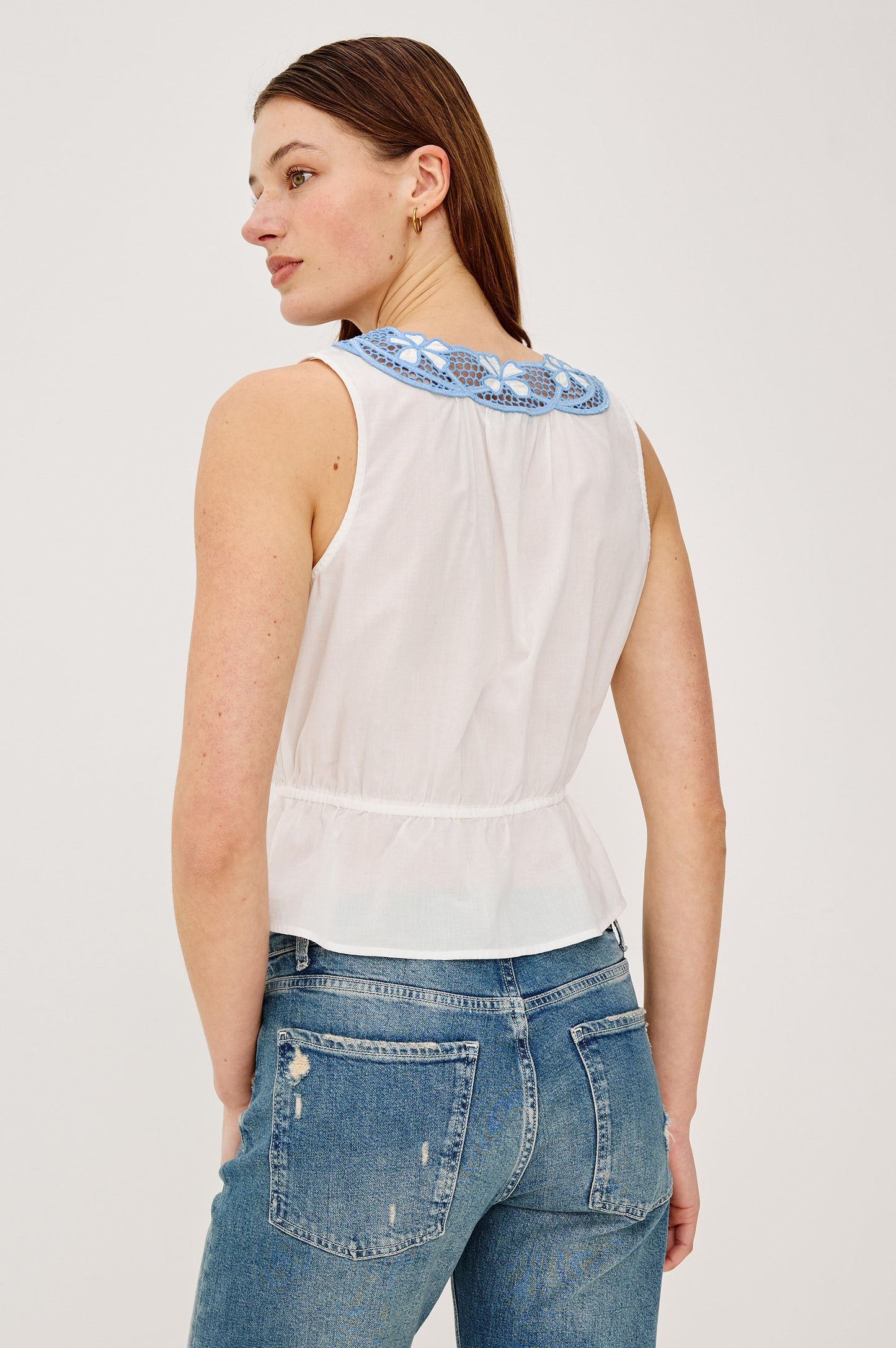 Woman wearing a white sleeveless top with blue embroidery