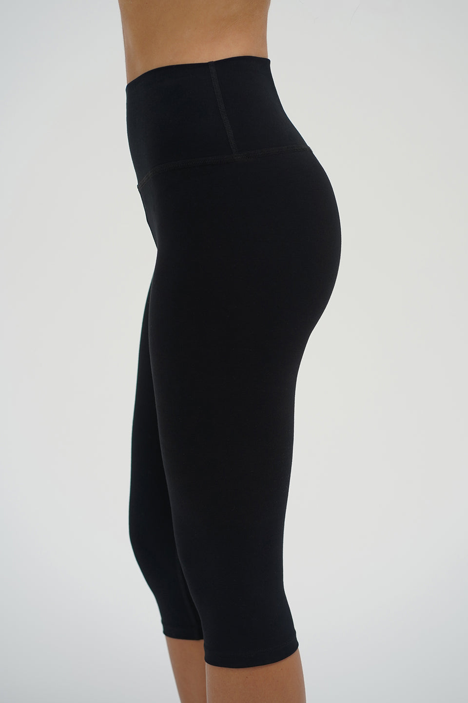 Black high-waisted capri leggings, cotton blend, modeled from side view against plain background.