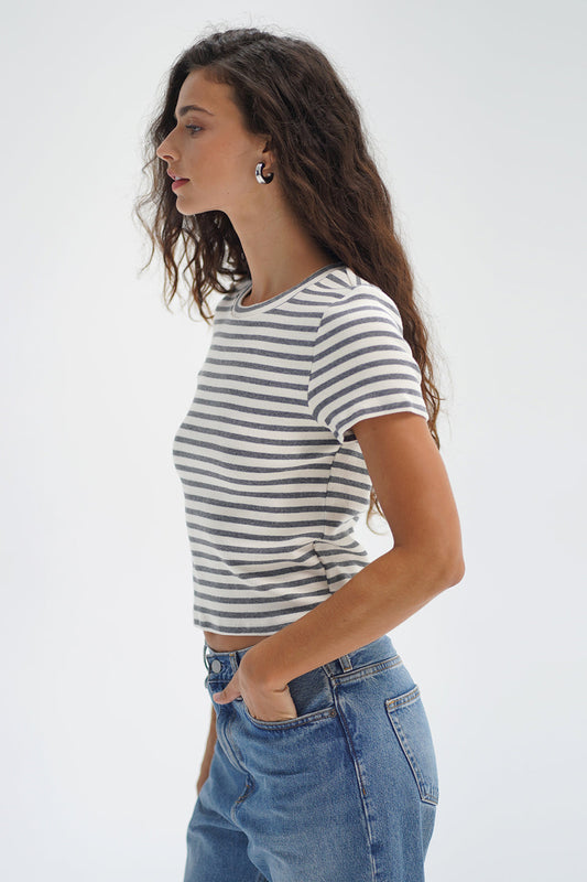 Woman with long wavy hair in a greyscale striped cotton tee, shown in profile against a plain white background.