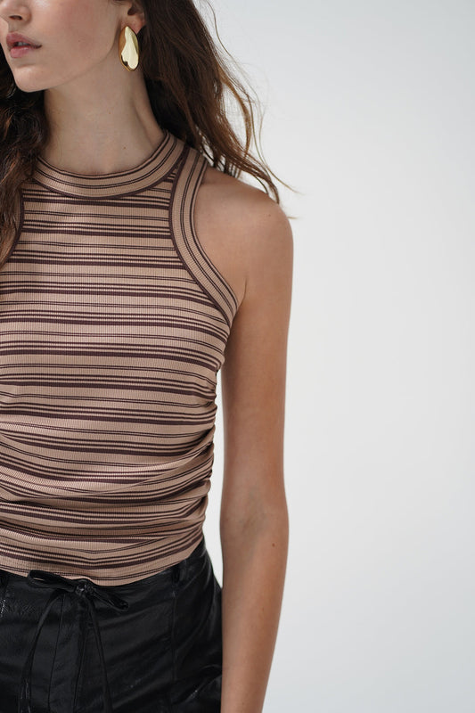 A woman wearing a ruched, sleeveless ribbed knit top with horizontal brown and beige stripes
