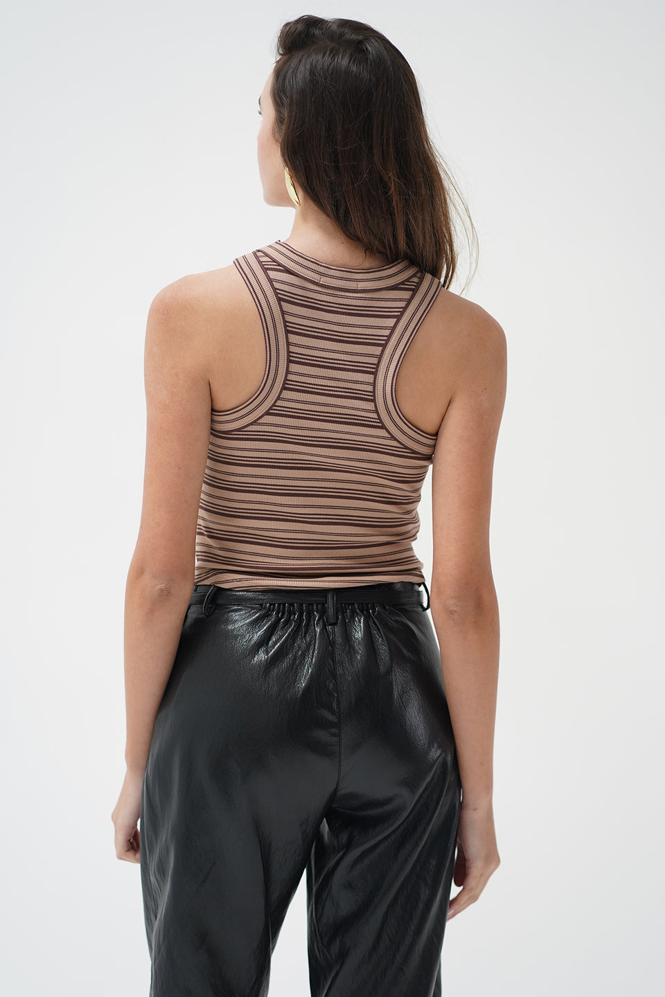 A woman wearing a ruched, sleeveless ribbed knit top with horizontal brown and beige stripes