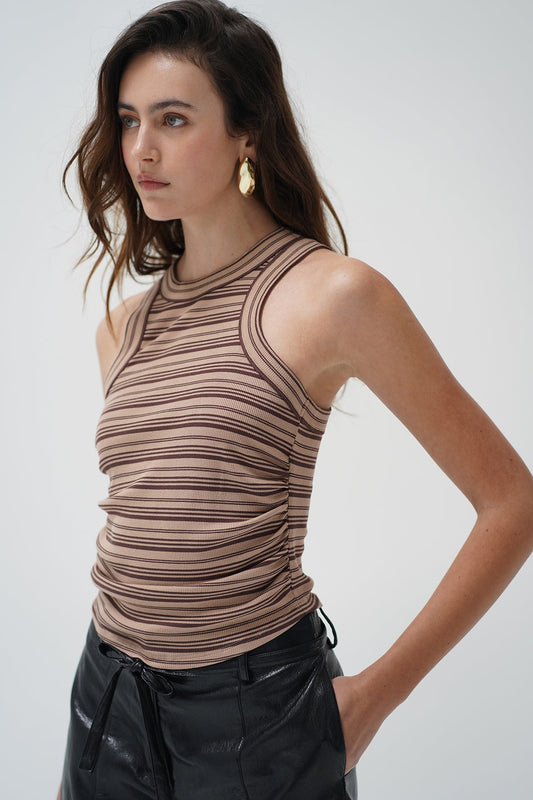A woman wearing a ruched, sleeveless ribbed knit top with horizontal brown and beige stripes