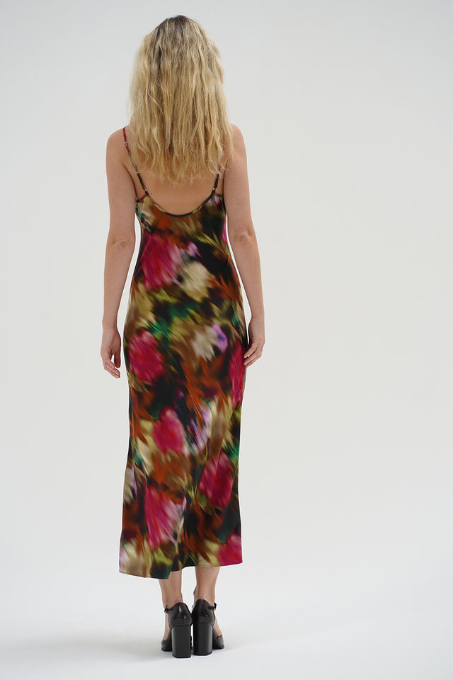 Woman in a blurred floral slip dress with black heels stands against a plain background. Dress is lightweight and sleeveless.