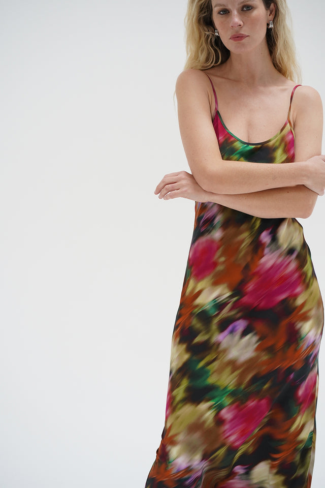 Woman in a floral slip dress with blurred print stands arms crossed against a plain white background.