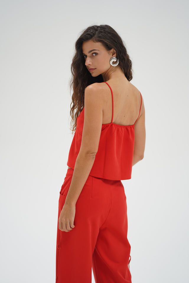 Woman with long wavy hair models a red chambray tank top, glancing over her shoulder against a plain backdrop.