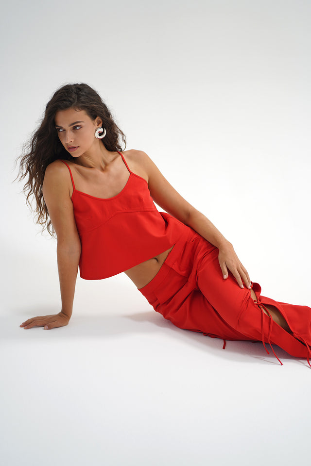 Woman with long wavy hair wears a red chambray tank top, standing against a plain white background.