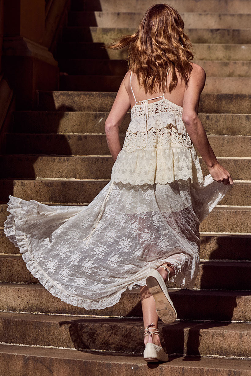 Woman in a cream lace maxi skirt runs up stone steps, red hair and skirt trailing behind her.