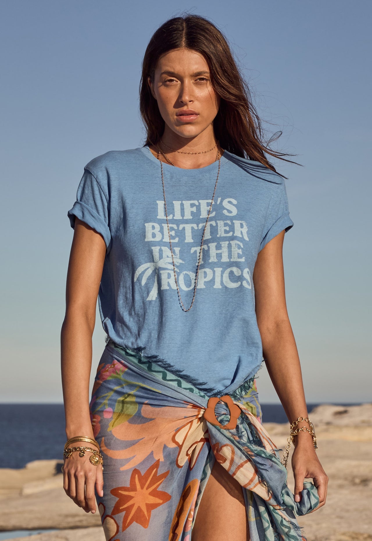 Woman by the ocean wears a blue cotton T-shirt and a lightweight floral sarong.