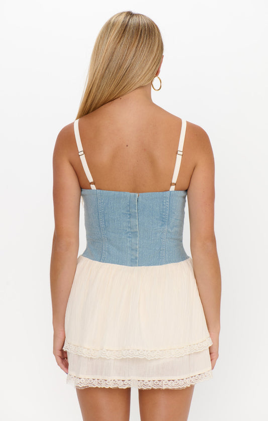 Back view of a woman in a light indigo and cream voile mini dress; long blonde hair visible.