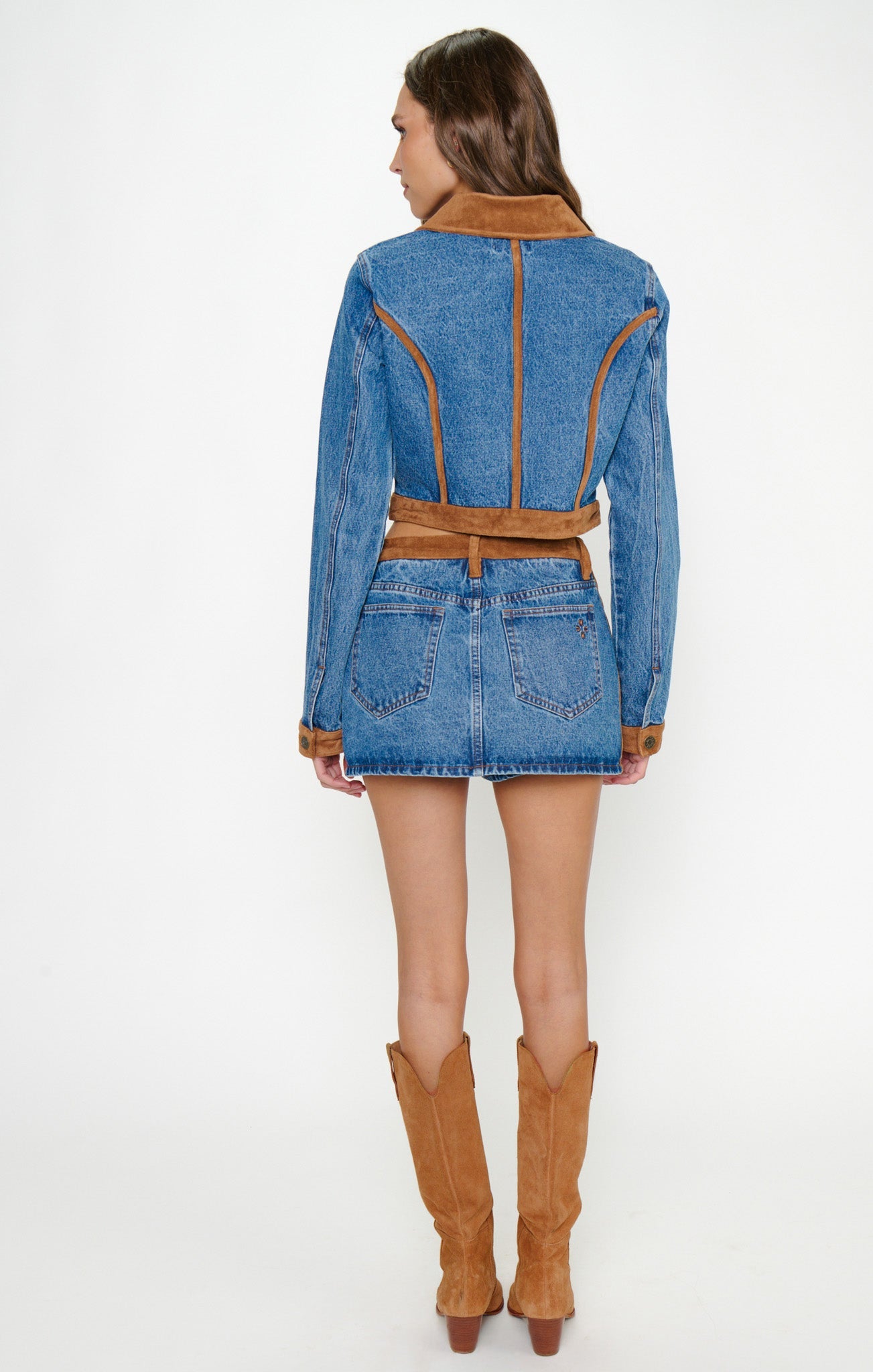 Woman in indigo faux fur-trimmed denim jacket, denim skirt, and Western knee-high boots, seen from behind.