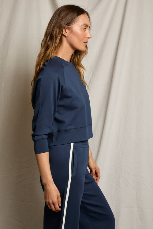 Woman wearing navy wide-leg pants, standing in profile against a beige fabric background.
