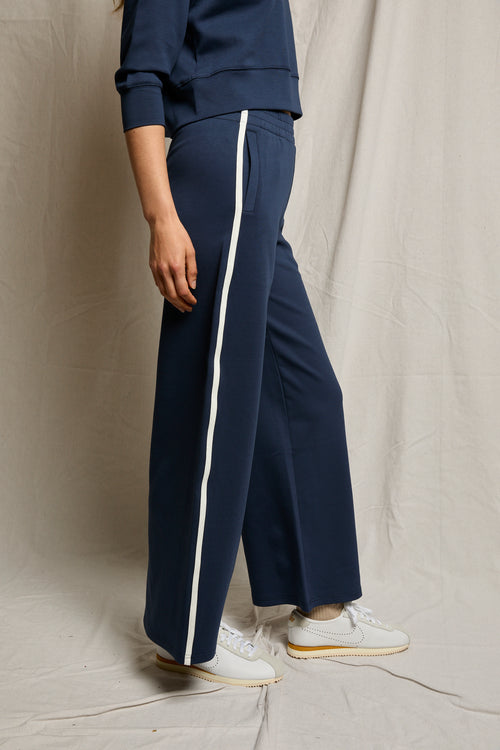 Individual in navy wide-leg pants and matching top, made of cotton, paired with white sneakers, standing in profile.